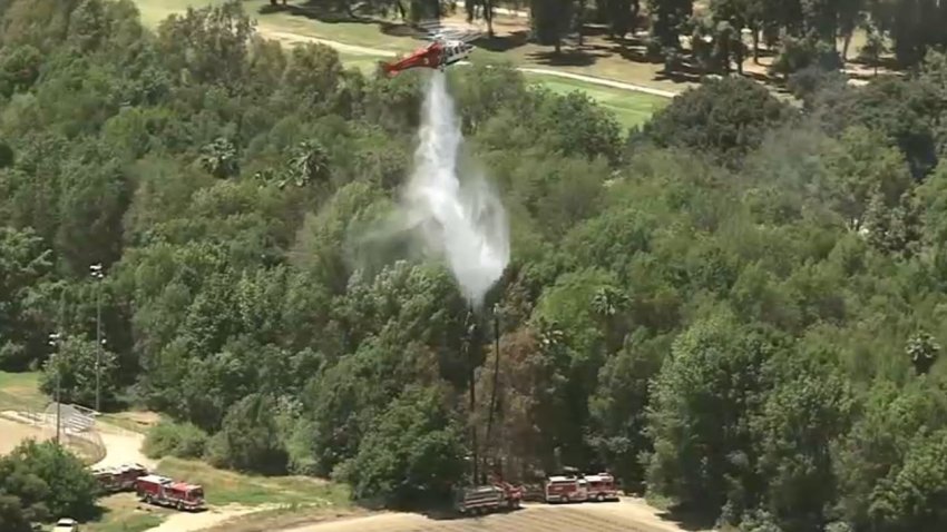 A helicopter drops water on a brush fire in the San Fernando Valley Monday June 24, 2024.