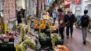 This photo taken on October 23, 2022 shows people looking at fruit and vegetables outside a supermarket along a covered shopping street in Tokyo.