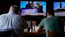 People sit in a local bar near the Fiserv Forum watching news