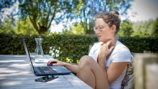 A young woman working at a table in a garden.