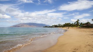 Pedestrians walk along a beach in Kihei, Maui County, Hawaii