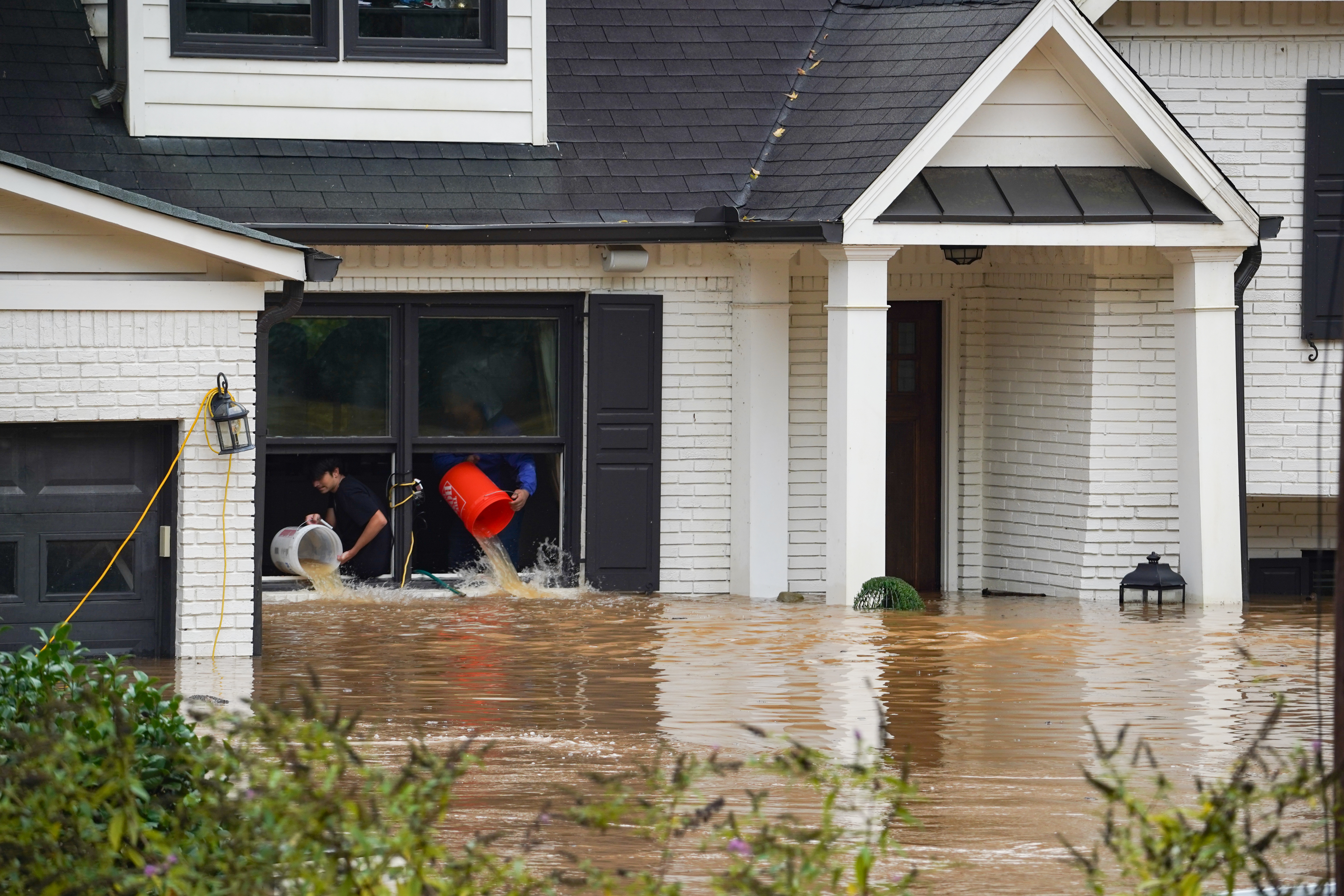 People toss buckets of water out of a home as the streets and homes are flooded near Peachtree Creek after hurricane Helene brought in heavy rains over night on September 27, 2024 in Atlanta, Georgia.