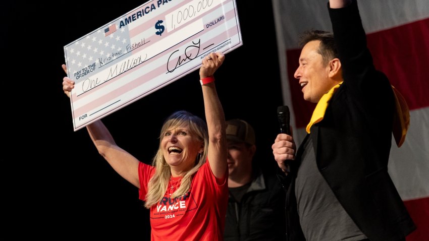 Elon Musk poses with a woman holding a check.