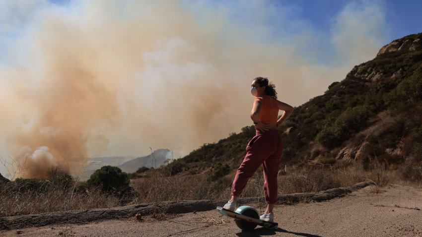 A person riding a Onewheel watches a mountainside burn as the Franklin Fire grows in Malibu, California, on December 10, 2024. A wind-fanned wildfire quickly spread early on Tuesday in Malibu, threatening homes and businesses in the coastal California community where many Hollywood elites reside. (Photo by DAVID SWANSON / AFP) (Photo by DAVID SWANSON/AFP via Getty Images)