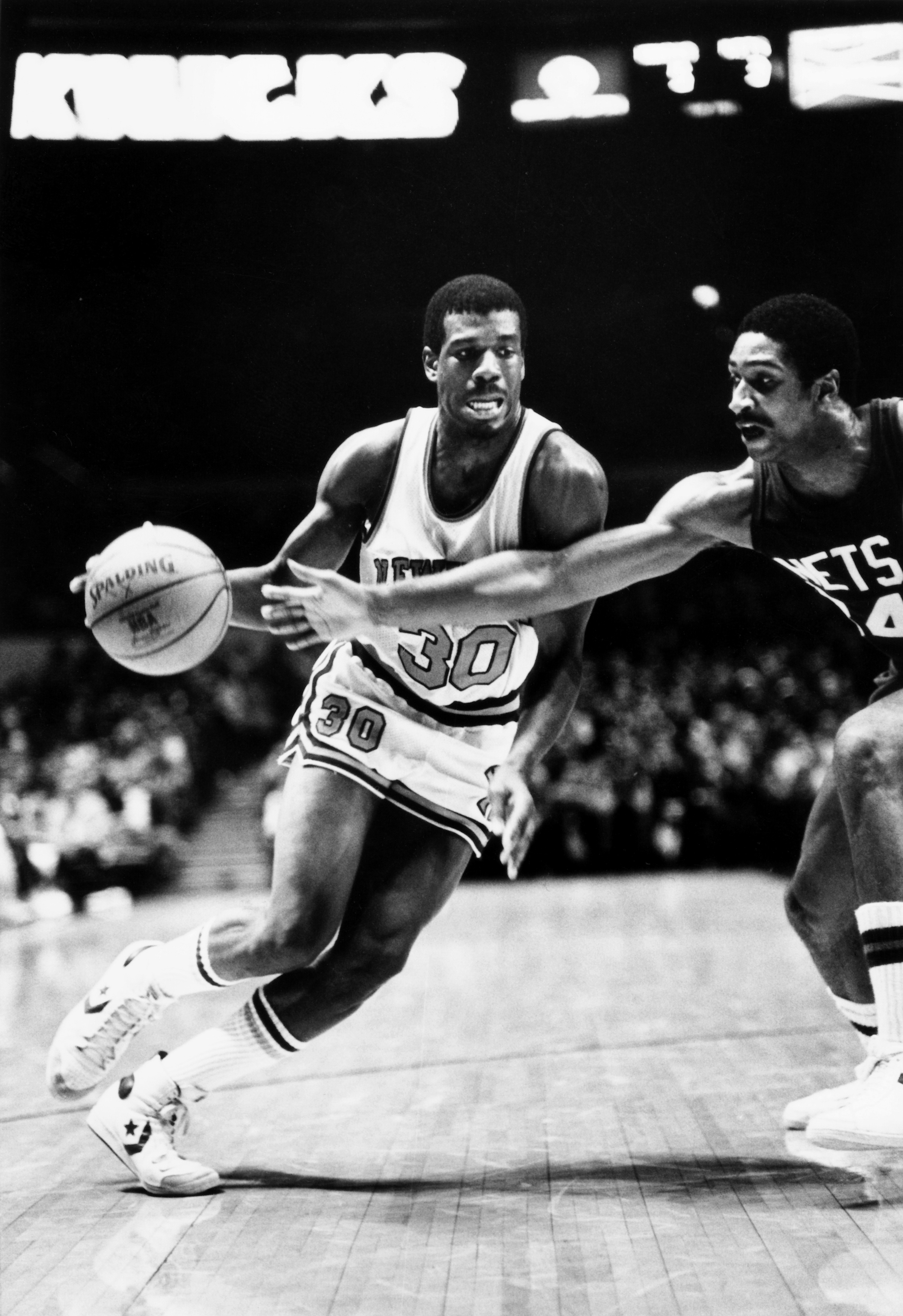 Bernard King in a white #30 New York Knicks jersey drives in the lane, dribbling the ball with his right hand at Madison Square Garden