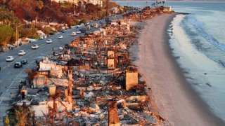An aerial view of repair vehicles at sunset passing near beachfront homes that burned in the Palisades Fire as wildfires cause damage and loss through the LA region on January 15, 2025 in Malibu, California. 