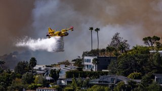 Pacific Palisades, CA – January 07: A Super SCooper plane drops water on the Palisades fire on Tuesday, Jan. 7, 2025 in Pacific Palisades, CA. (Brian van der Brug / Los Angeles Times via Getty Images)