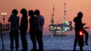 People gather at the beach after sunset with offshore oil and gas platform Esther in the distance on January 5, 2025 in Seal Beach, California. 