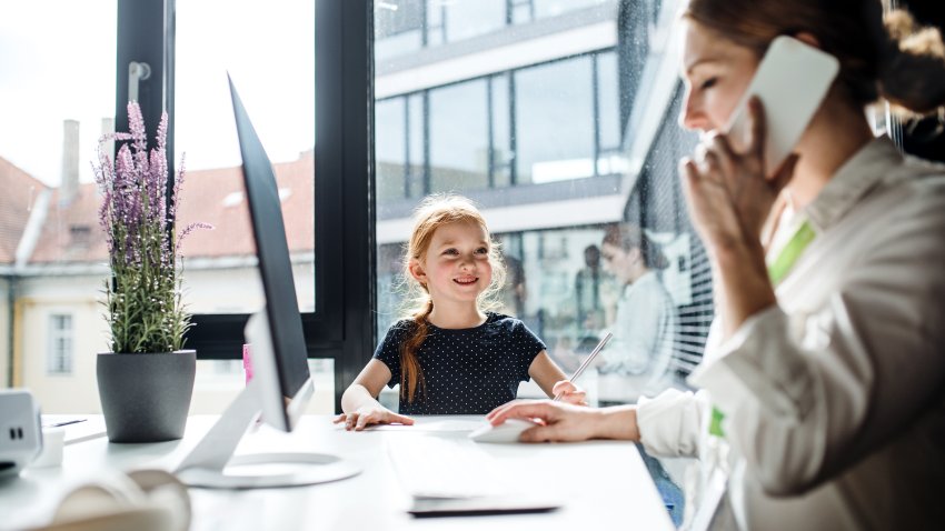 A businesswoman with a small daughter sitting in an office, working.