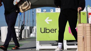 Travelers walk past a sign pointing toward the Uber ride-share vehicle pickup area at Los Angeles International Airport in Los Angeles on Feb. 8, 2023.