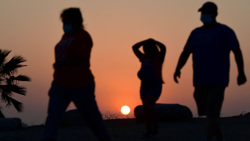 The sun sets behind people walking an afternoon hike in Los Angeles, California on July 12, 2021. – Wildfires were burning across more than one million acres of the western United States and Canada on July 12, 2021, as scorching temperatures held their grip on areas reeling from a brutal weekend heat wave. (Photo by Frederic J. BROWN / AFP) (Photo by FREDERIC J. BROWN/AFP via Getty Images)