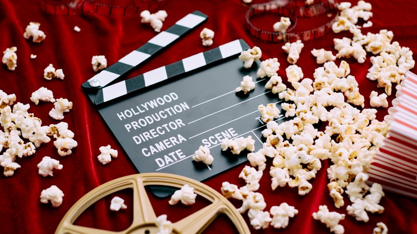 Clapperboard, film reel, film and spilled popcorn on red satin background. Concept of film industry, cinema, entertainment, and Hollywood.