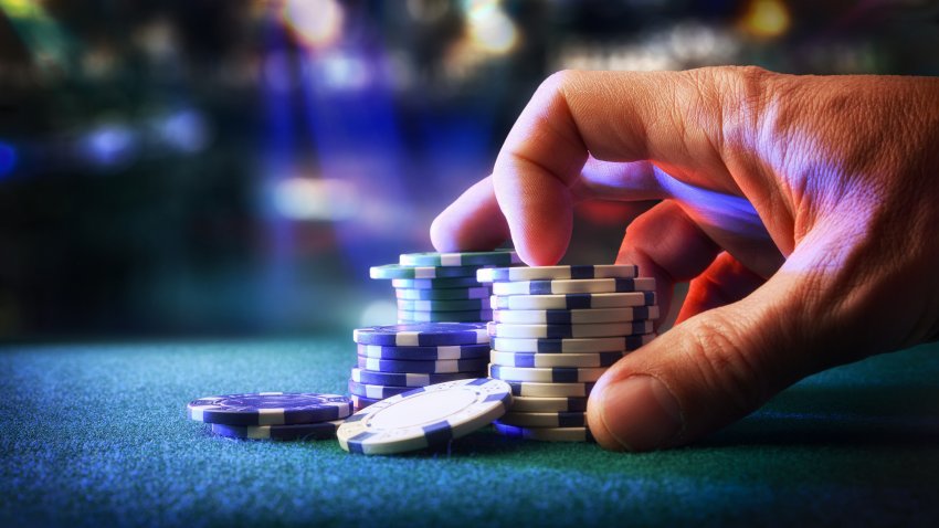 Hand betting game chips on felt mat with game room in the background. Front view.