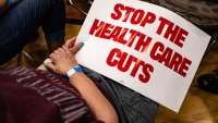 An attendee holds a “Stop The Health Care Cuts” sign during a town hall in Lansing, Michigan, US, on Friday, June 6, 2025. Republicans are betting they can win the semantic battle over the future of Medicaid, with a multi-trillion dollar tax bill at stake, while Democrats view the cuts as a welcome talking point to attack the president’s agenda. Photographer: Emily Elconin/Bloomberg via Getty Images
