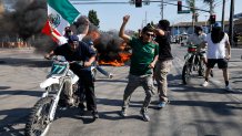 Los Angeles, CA - June 07: Anti-ICE protesters celebrate in front of a burning car in the middle of the intersection of Atlantic Ave. and E Alondra Blvd. during ICE protests on Saturday, June 7, 2025 in Los Angeles, CA. (Carlin Stiehl / Los Angeles Times via Getty Images)