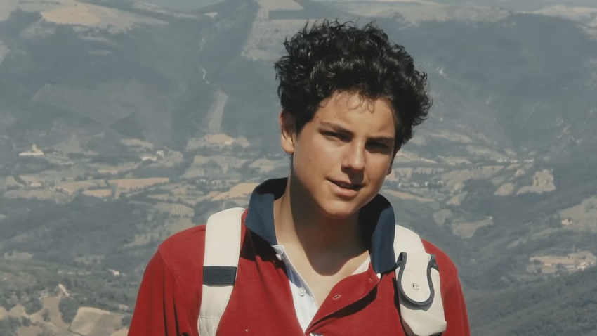 Photo of Carlo Acutis with landscape behind him