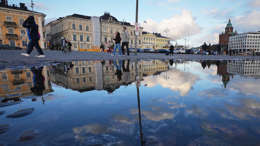 People walking along the square are reflected in a puddle in Helsinki, Finland, Friday, Nov. 14, 2025.