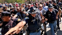 In this Tuesday, July 19, 2016 file photo, Alex Jones, second from right, an American conspiracy theorist and radio show host, is escorted by police out of a crowd of protesters after he said he was attacked in Public Square in Cleveland, during the second day of the Republican convention.