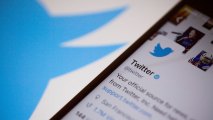 The Twitter Inc. logo is seen behind an Apple Inc. iPhone 6s displaying the company